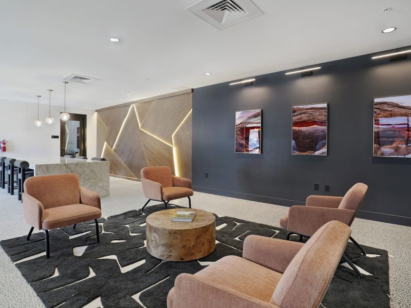 Modern lounge with four tan chairs, a round table, wall art, and geometric lighting on dark accent wall at The Hendrey.