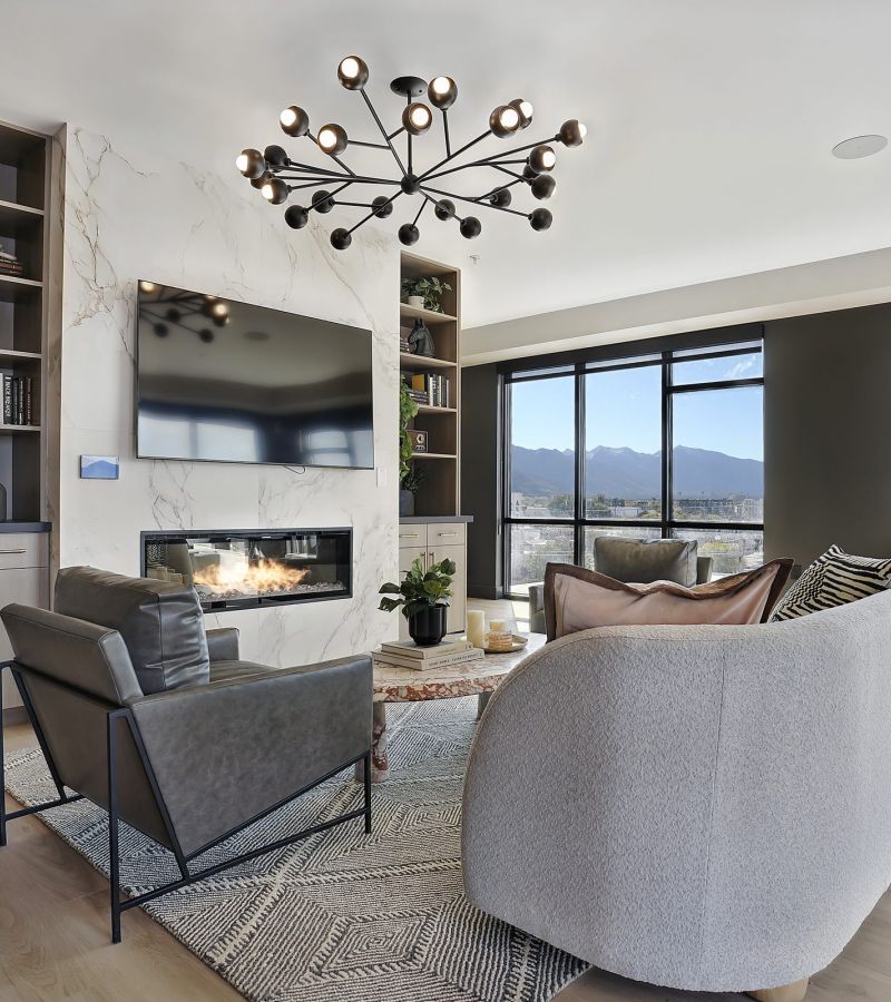 Modern living room with large windows, light wood floors, cozy seating, and a statement chandelier at The Hendrey.