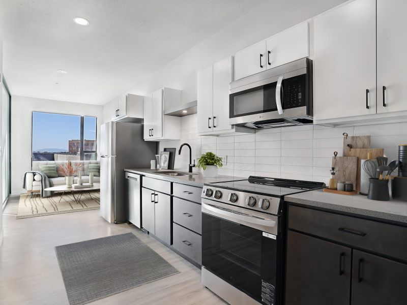 Modern kitchen with black and white cabinets, stainless steel appliances, and a view into a bright living room at The Hendrey.