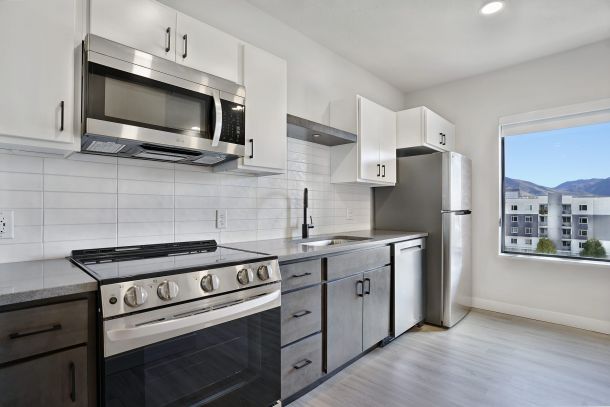 Modern kitchen with stainless steel appliances, white cabinets, gray lower cabinets, and a large window at The Hendrey.