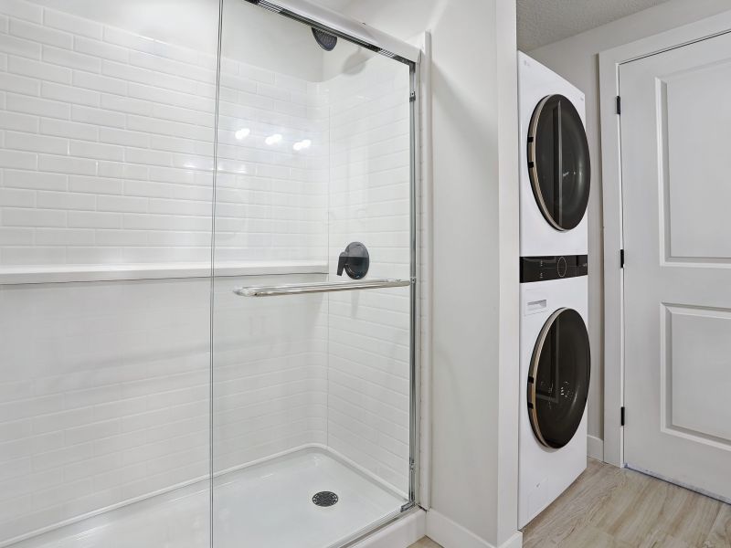 Modern bathroom with a glass shower and a stacked washer and dryer next to a white door at The Hendrey.