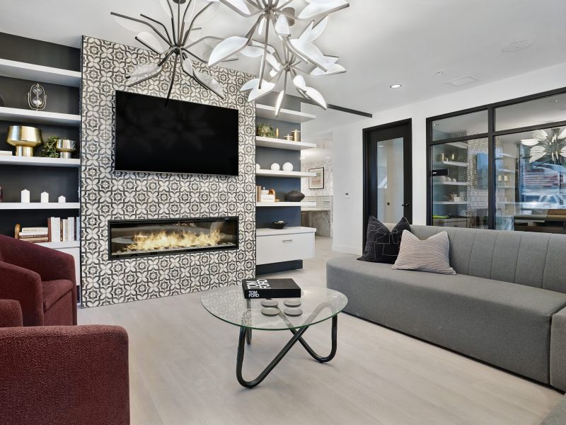Modern living room with patterned fireplace, wall-mounted TV, red chairs, gray sofa, and glass coffee table at The Hendrey.