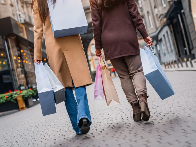 Two women walking on a city street, carrying several shopping bags in their hands.
