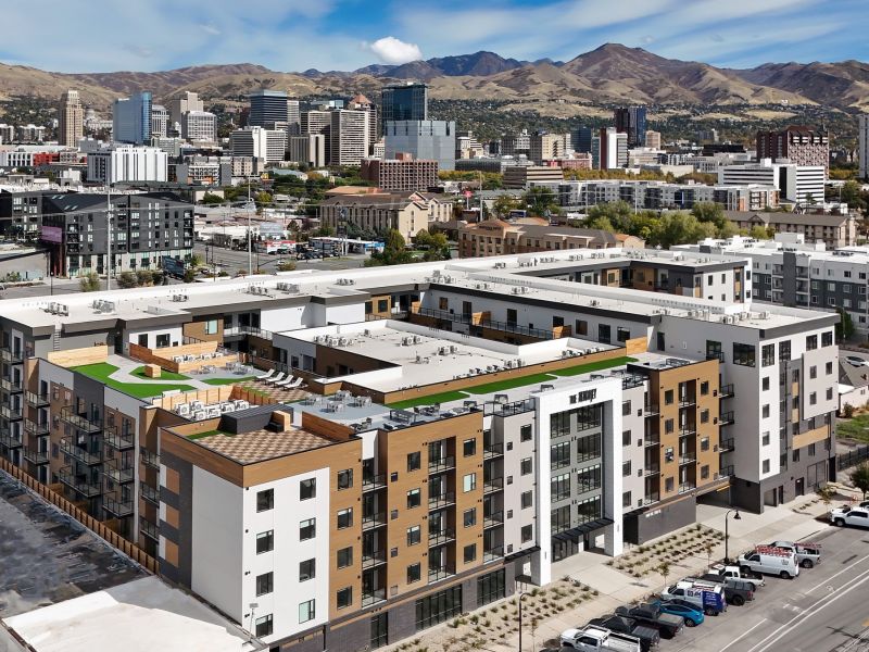 A modern apartment complex with a rooftop area, set against a city skyline and mountains in the background at The Hendrey.
